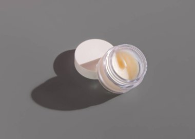 Gri arka planda boş bir kapağı olan açık dudak kremi kavanozu, yakın plan sert gölge, kozmetik model, negatif alan. Ruj bakım için cilt bakımı ürünü, asgari estetik