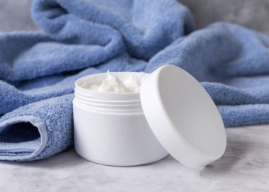 Mavi banyo havlusunun yanında boş kapaklı beyaz krema kavanozu, yakın plan, marka ambalaj modeli. Günlük yüz bakımı ve spa prosedürleri için doğal bitkisel kozmetik ürünleri, kopyalama alanı