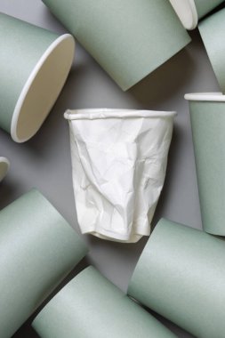 Tek kullanımlık yeşil kağıt bardaklar ve buruşmuş beyaz bardaklar gri üstte, fotokopi alanı ile modellenmiş. Boş karton kahve fincanları düz yerde. Tüketim kavramı 
