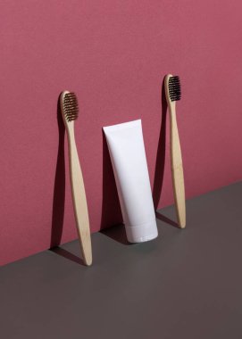 Blank toothpaste tube and bamboo toothbrushes on a grey and dark red closeup, hard shadow, cosmetic mockup, negative space. Healthcare natural products, minimal aesthetic clipart