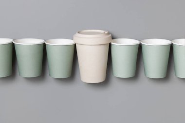 Tek kullanımlık yeşil kağıt bardaklar ve yeniden kullanılabilir bambu kahve fincanı gri bir üst görünüm, fotokopi alanı ile modelleme. Boş kahve fincanları düz yerde. Plastik ve sürdürülebilir yaşam tarzı kavramı yok 