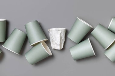 Tek kullanımlık yeşil kağıt bardaklar ve buruşmuş beyaz bardaklar gri bir üst görünüm, fotokopi alanı ile modelleme. Boş karton kahve fincanları düz yerde. Plastik ve sürdürülebilir yaşam tarzı kavramı yok 