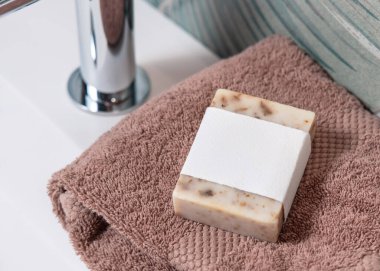 Yeşil tropikal banyodaki leğenin üzerindeki kahverengi katlanmış havluların üzerinde boş etiketli bej sabun kalıbı, fotokopi alanı ile paketleme. Günlük hijyen için markasız doğal bitki ürünü.