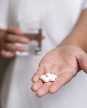 Beyaz tişörtlü bir kadın, elinde beyaz haplar, elinde su bardakları. Kadın ya da erkek beslenme takviyesi ya da vitamin alıyor. Sağlık hizmetleri kavramı