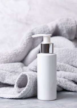 Açık gri havlunun yanında beyaz boş bir pompa şişesi banyo manzaralı, marka ambalaj modeli, kopyalama alanı. Günlük cilt bakımı için doğal bitkisel losyon ya da krem