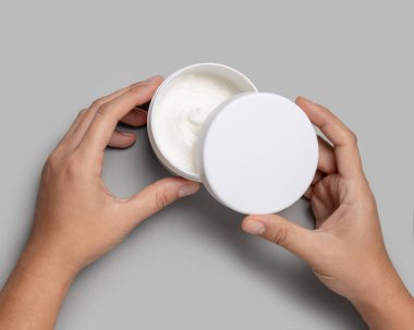 Doğal manikürlü, gri arka plan manzarası üzerinde boş kapağı olan kadın elleri, kozmetik modelleme. Vücut veya yüz bakımı için organik kozmetik ürünleri, minimum estetik