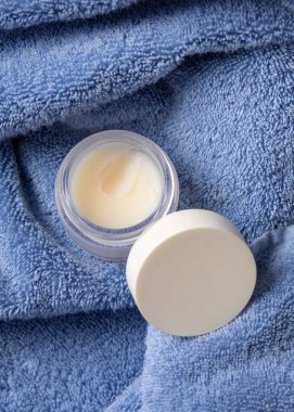 Mavi banyo havlusunun üstünde boş kapaklı dudak kremi kavanozu, kozmetik ambalajlama, kopyalama alanı. Lipcare güzellik ürünleri erkekler ve kadınlar için günlük kişisel bakım