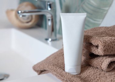 Kahverengi katlanmış havlulara beyaz krema sıkma tüpü yeşil tropikal banyodaki leğene yakın, ambalaj modeli. Fotokopi alanı ile markasız doğal bitki kozmetikleri. Spa ve sağlık konsepti