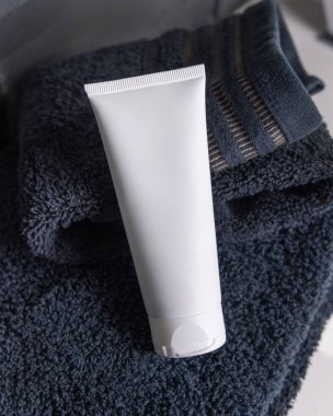 Siyah katlanmış havluların üzerine beyaz krem sıkma tüpü koyu gri erkeksi tuvaletteki leğenin üzerine yakın çekim, ambalaj modeli. Fotokopi alanı ile markasız doğal bitki kozmetikleri. Spa ve sağlık konsepti