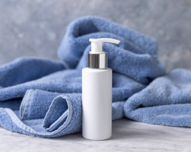 Banyoda mavi havlunun yanında beyaz boş bir pompa şişesi, marka ambalaj modeli. Doğal el yapımı kozmetik ürünü - günlük yüz veya el bakımı için krem, losyon veya sabun, kopyalama alanı