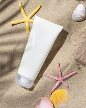 Beyaz, boş bir krem tüpü, kumlu plaj manzaralı deniz kabukları, sert gölgeler. Güneş kremi maketi. Güneş banyosuyla korunan yaz tatili