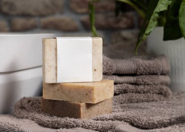 Açık kahverengi havluların üzerinde boş etiket olan sabun barı, banyodaki yeşil bitki ve damar havzasının yanında, yakın plan, marka ambalajlama modeli. Erkekler için hijyen ürünü