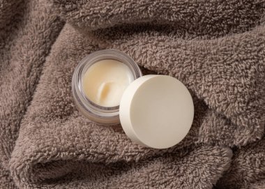 Açık dudak kremi kavanozu. Açık kahverengi banyo havlusunun üstü görünüyor. Kozmetik ambalaj modeli, kopyalama alanı. Lipcare güzellik ürünleri erkekler ve kadınlar için günlük ruj bakım ve kişisel bakım