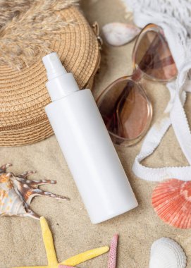 Beyaz, boş bir sprey şişesi, güneş gözlüğü, havlu, kumlu bir sahilde deniz yıldızı ve deniz kabuğu. Güneş kremi kozmetikleri