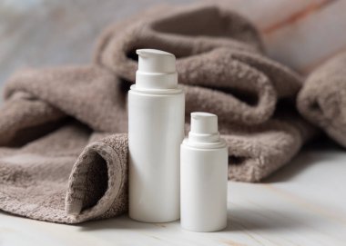 Kahverengi havlunun yanında beyaz boş bir pompa krem şişesi yakın plan, marka ambalaj modeli. Doğal bitkisel kozmetik ürünü - günlük yüz bakımı için krem, losyon veya köpük, kopyalama alanı