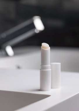 Açık dudak merhemi çubuğu, boş kapaklı, koyu gri, modern, erkeksi banyoda musluk, ambalaj modeli. Ruj bakımı için doğal markasız kozmetik ürünleri, kopyalama alanı