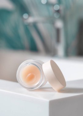 Yeşil tropikal banyoda musluğu olan lavabo kapaklı beyaz, boş dudak kremi kavanozu açıldı. Paketleme modeli. Doğal ruj bakım ürünüyle hayat dolu bir sahne.