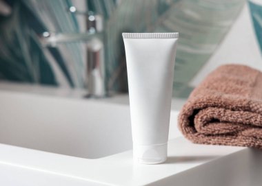Kahverengi katlanmış havluların yanında beyaz krem sıkma tüpü yeşil tropikal banyodaki leğene yakın, ambalaj modeli. Fotokopi alanı ile markasız doğal bitki kozmetikleri. Spa ve sağlık konsepti