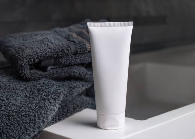 Siyah katlanmış havluların yanında beyaz krem sıkma tüpü koyu gri erkek banyosunda, yakın çekim, ambalaj modeli. Fotokopi alanı ile markasız doğal bitki kozmetikleri. Spa ve sağlık konsepti