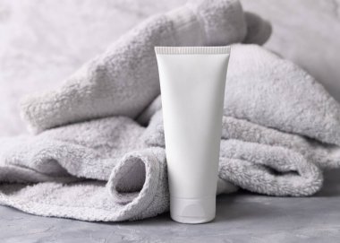 Banyonun üst görüntüsünde açık gri havlunun yanında beyaz, boş kozmetik sıkma krem tüpü, marka ambalaj modeli. Günlük yüz bakımı için doğal bitkisel kozmetik ürünü, kopyalama alanı