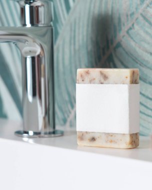 Yeşil tropikal banyodaki lavabonun yanındaki boş muslukta bej sabun barı, fotokopi alanı ile ambalajlama. Günlük hijyen için markasız doğal bitki ürünü.