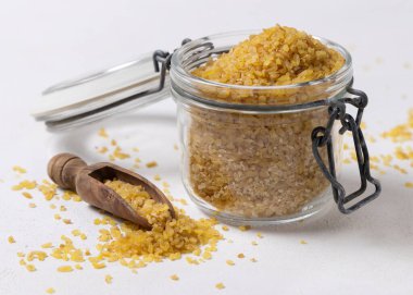 Cam kavanozu aç pişmemiş sarı bulgur buğdayı ve yakın plan ahşap bir kepçe ile. Orta Doğu kuzeni. Sağlıklı beslenme için organik süper yiyecekler. Eski alternatif tahıl tohumları