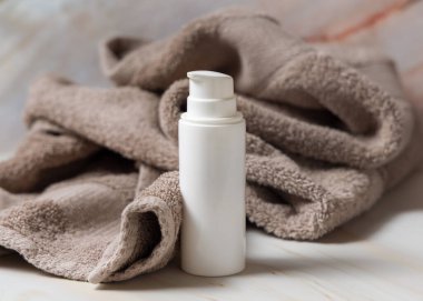 Banyodaki kahverengi havlunun yanında beyaz boş bir pompa krem şişesi, marka ambalaj modeli. Doğal bitkisel kozmetik ürünü - günlük yüz bakımı için krem, losyon veya köpük, kopyalama alanı