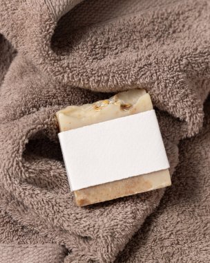 Açık kahverengi banyo havlusunun üstünde boş etiketli bej bitkisel sabun, üst görünümü, ambalaj modeli, kopyalama alanı. Günlük temizlik ve cilt bakımı için doğal el yapımı sabun.