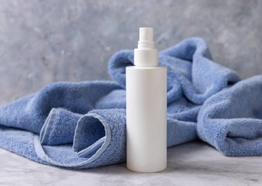 Banyoda mavi havlunun yanında beyaz, boş bir sprey boya şişesi, marka ambalaj modeli. Doğal el yapımı kozmetik ürünü - toner veya günlük yüz veya saç bakımı için emülsiyon, kopyalama alanı