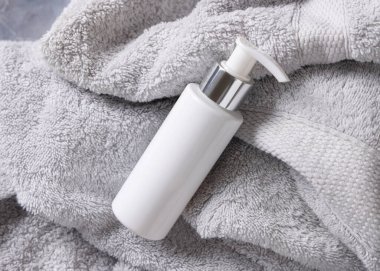 Beyaz boş kozmetik bir pompa krem şişesi açık gri havlu üzerine banyo üst görünümü, marka ambalaj modeli. Günlük yüz bakımı için doğal bitkisel kozmetik ürünü, kopyalama alanı