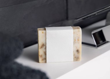 Modern koyu gri banyoda lavabonun yanında boş etiketli bej el yapımı sabun ve siyah banyo havlusu. Günlük erkek hijyeni için doğal bitkisel ürün