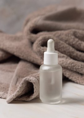 Açık kahverengi banyo havlusunun yanında pipeti olan cam damlatan şişeyi yakın plan, ambalaj modeli, kopyalama alanı. Yüz bakımı ve spa prosedürleri için doğal organik kozmetik ürünü - serum veya öz