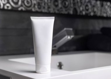 Modern musluğun yanındaki beyaz krem tüpü koyu gri, erkeksi tuvalette kapanıyor, ambalaj modeli. Kopya alanı olan doğal markasız kozmetik ürünler. Spa ve sağlık konsepti