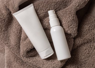 Beyaz, boş, sıkılmış krem tüpü ve kahverengi havluyla banyo manzaralı sprey şişesi, marka ambalaj modeli, fotokopi alanı. Yüz bakımı ve spa işlemleri için doğal el yapımı kozmetik ürünü