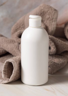 Kahverengi banyo havlusunun yanında losyon, sabun ya da şampuan içeren beyaz, boş bir kapak şişesi yakın plan, kopyalama alanı, maket. Günlük vücut bakımı ve kaplıca işlemleri için doğal organik kozmetik ürünleri