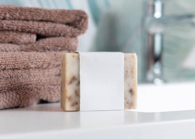 Yeşil tropikal banyodaki leğenin üzerinde kahverengi katlanmış havluların yanında boş etiketli bej sabun kalıbı, fotokopi alanı ile paketleme. Günlük hijyen için markasız doğal bitki ürünü.