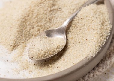 Çiğ fonio tohumları tabakta, beyaz masada metal bir kaşık var. Afrika 'nın antik sahte tahtaları. Organik süper yiyecekler. Sağlıklı gıda konsepti. Glütensiz alternatif tohumlar