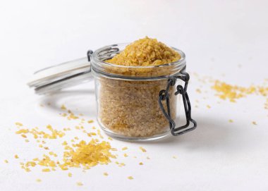 Açık cam kavanoz çiğ, pişmemiş sarı bulgur tanecikleri beyaz masa üzerinde, yakın plan, kopyalama alanı. Orta Doğu kuzeni. Sağlıklı beslenme için organik süper yiyecekler. Eski alternatif mısır gevreği. tohumlar