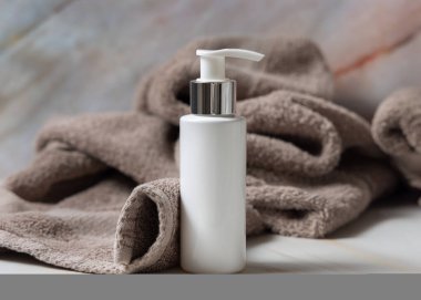 Banyodaki kahverengi havlunun yanında beyaz boş bir pompa krem şişesi, marka ambalaj modeli. Doğal bitkisel kozmetik ürünü - günlük yüz bakımı için krem, losyon veya köpük, kopyalama alanı