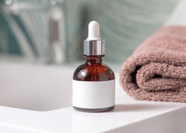 Kahverengi havluların yanında pipet ve yeşil tropikal banyodaki havuzun üstünde musluk olan kahverengi cam damlalar. Etiket modeli. Kopya alanı olan doğal markasız kozmetik ürünler. Spa konsepti
