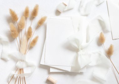 Kurumuş tavşanın kuyruğundaki beyaz ipek kurdelelerle bağlanmış boş kartlar beyaz, model. Boho Pastel Romantik Flatlay. Parti tasarımı ya da düğün kırtasiyesi için bohem ya da doğa kartlarına yakın