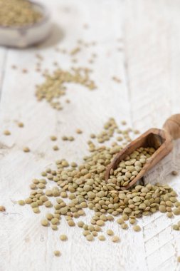 Beyaz masadaki kurutulmuş yeşil mercimek kepçesiyle dolu tahta kepçe. Sağlıklı vejetaryen yiyecekler, bitkisel protein kaynakları. Geleneksel Akdeniz çiğ kuzen malzemesi