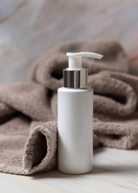 Banyodaki kahverengi havlunun yanında beyaz boş bir pompa krem şişesi, marka ambalaj modeli. Doğal bitkisel kozmetik ürünü - günlük yüz bakımı için krem, losyon veya köpük, kopyalama alanı