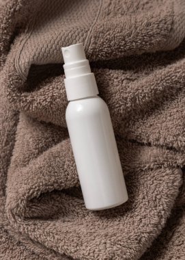 Kahverengi havlunun üzerinde beyaz, boş sprey krem şişesi banyo manzaralı, marka ambalaj modeli. Doğal bitkisel kozmetik ürünü - günlük yüz bakımı için krem, losyon veya köpük, kopyalama alanı