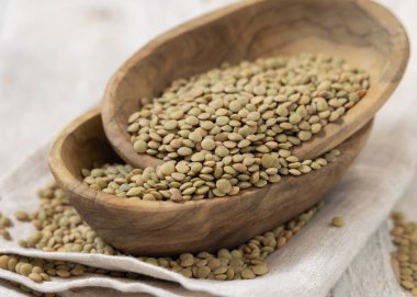 Tahta kaseler, beyaz masada kurutulmuş yeşil mercimeklerle dolu. Sağlıklı vejetaryen yiyecekler, bitkisel protein kaynakları. Geleneksel Akdeniz çiğ kuzen malzemesi