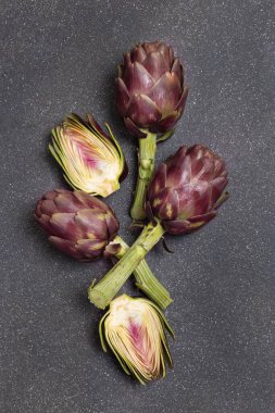 Tamamı ve yarıya bölünmüş çiğ mor Roma enginarları gri beton masa üst görüşü, kopyalama alanı. Çiftçi pazarından taze sebzeler pişmeye hazır. İtalyan kuzeni içeriği