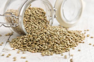 Beyaz masada içi kurutulmuş yeşil mercimek dolu cam kavanoz. Sağlıklı vejetaryen yiyecekler, bitkisel protein kaynakları. Geleneksel Akdeniz çiğ kuzen malzemesi