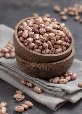 Gri masadaki peçetenin üzerinde kurumuş fasulye dolu ahşap kase. Sağlıklı vejetaryen yemekleri, protein kaynakları. Geleneksel Latin Amerikalı kuzen malzemesi