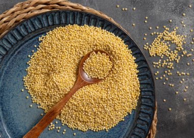 Mavi tabak çiğ sarı darı tahılı ve tahta kaşıkla gri masa manzaralı. Organik inci kabuklu darı. Eski, sağlıklı süper yiyecekler. Glütensiz alternatif tohumlar