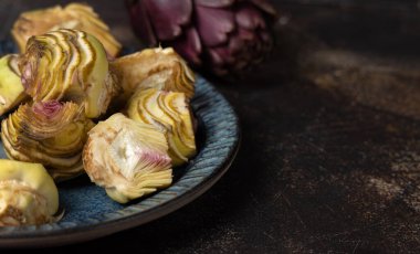 Koyu kırsal masadaki çiğ enginar kalpleriyle dolu bir tabak. Yakın plan, kopyalama alanı. Çiftçi pazarından alınmış taze sebzeler. Temizlik yapıyor ve yemek yapmaya hazırlanıyor. İtalyan kuzeni.